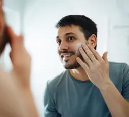 A young man looking in the mirror while applying a skincare product.