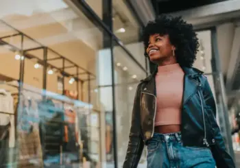 A woman smiling as she walks past a clothes shop window.