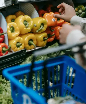 A shopper reaching for vegetables on a supermarket shelf.